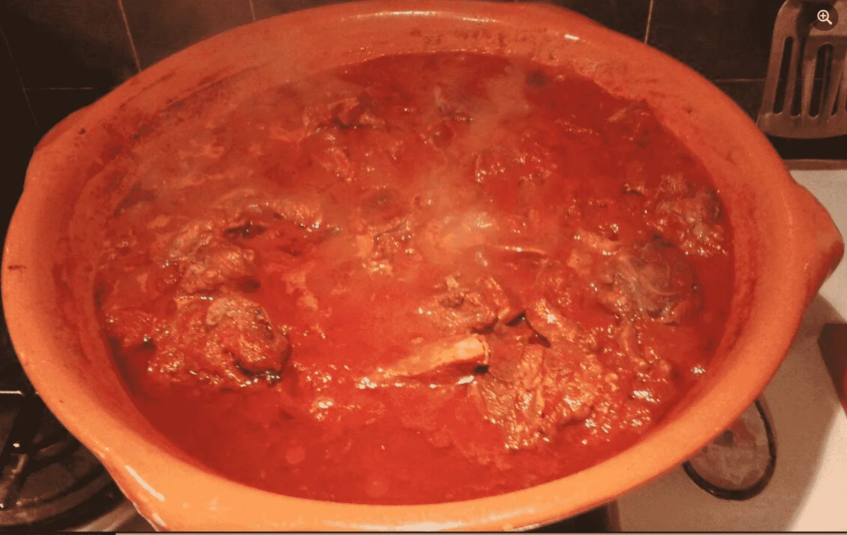 Sicilian lamb stew in terracotta pot with tomato sauce and bay leaves