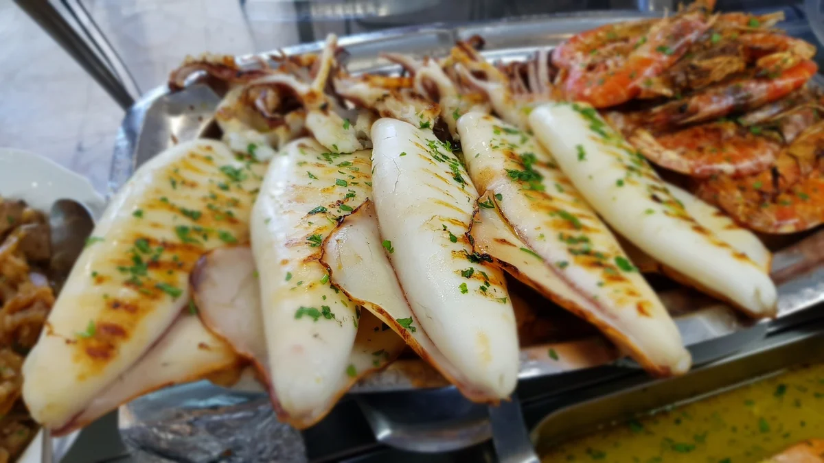 Grilled Sicilian-style calamari with salmoriglio and lemon slices on a ceramic plate