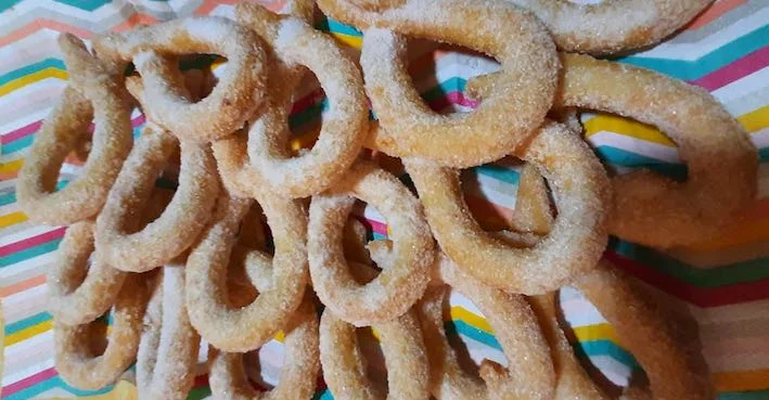 Cuḍḍureḍḍi di Carnevale dorati e spolverati di zucchero e cannella su un piatto colorato siciliano