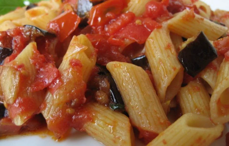 Pasta con le melanzane e pomodorini servita su piatto in ceramica siciliana decorata