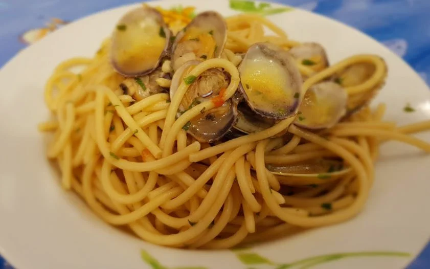 Pasta con le vongole servita in un piatto bianco, con prezzemolo fresco e gusci di vongole aperti