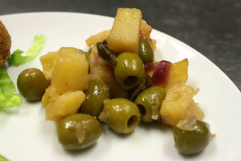 Patate apparecchiate alla siracusana con olive e capperi servite in tegame di terracotta