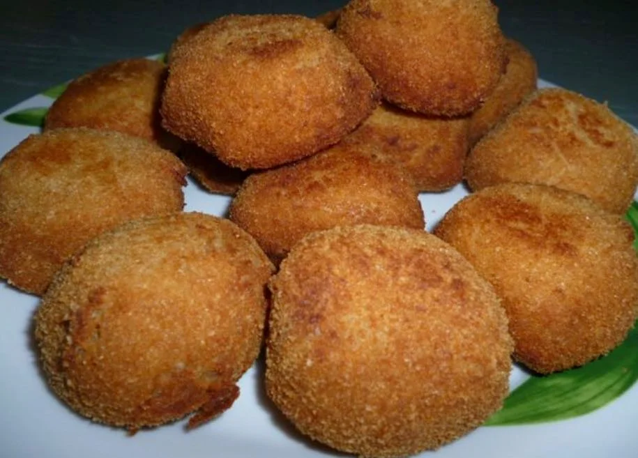 Polpette di tonno e ricotta dorate e croccanti servite su piatto di ceramica siciliana con limone e prezzemolo