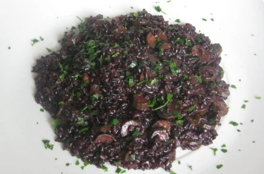 Risotto al nero di seppia alla siciliana servito in piatto bianco con scorza di limone e prezzemolo fresco