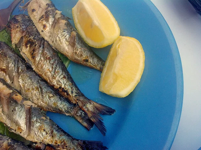 Sarde alla brace dorate e croccanti servite su piatto di ceramica siciliana con limone