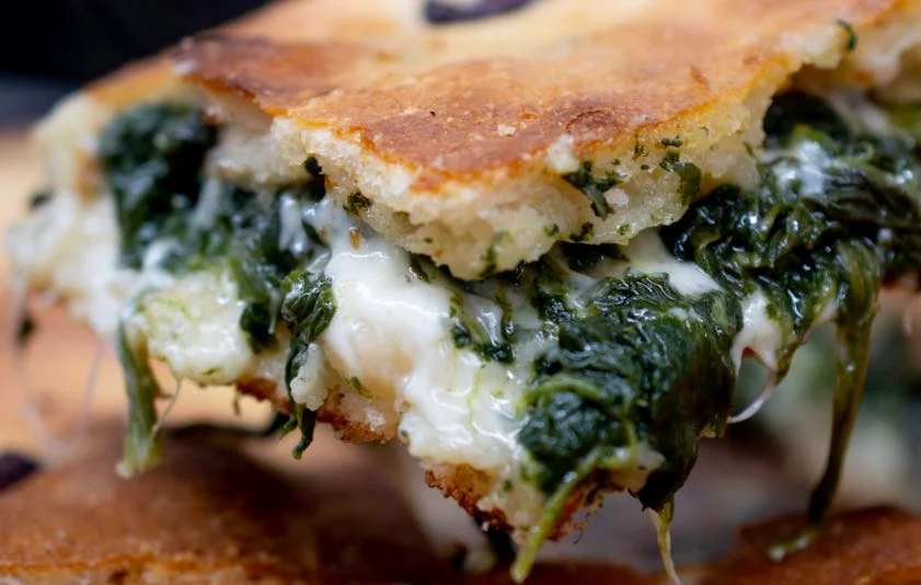 Schiacciata nissena con tuma e spinaci dorata e fragrante, tagliata a fette su un tagliere in legno