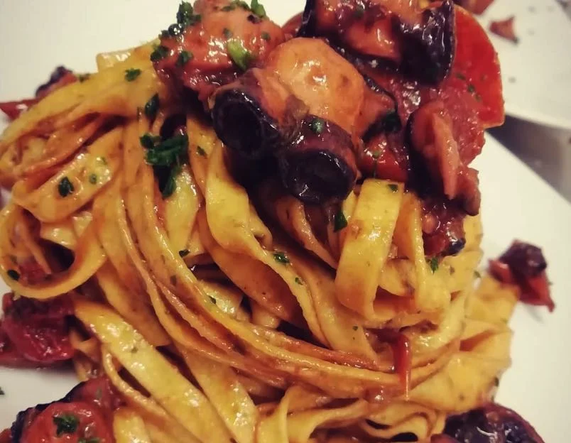 Tagliatelle con polpo servite su piatto in ceramica siciliana con basilico fresco e pomodori