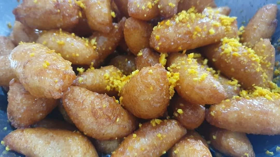 Zeppole di riso catanesi dorate e ricoperte di miele su piatto di ceramica siciliana